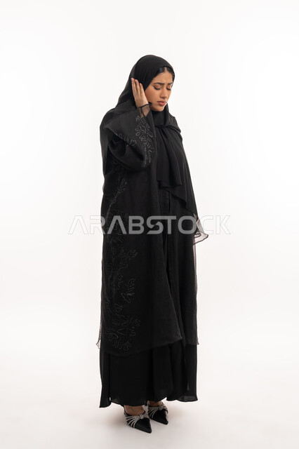 طلب العلاج و المساعده، تسوس الأضراس وإلتهاب اللثه، بورتريه من الجانب لامرأه عربيه خليجيه اماراتية محجبة ترتدي عباءة سوداء تضع يدها على خدها بإيماءات تدل على الشعور بألم الأسنان، الحاجه لزيارة الطبيب، شابة سعودية مريضة، صورة لكامل الجسم، خلفية بيضاء