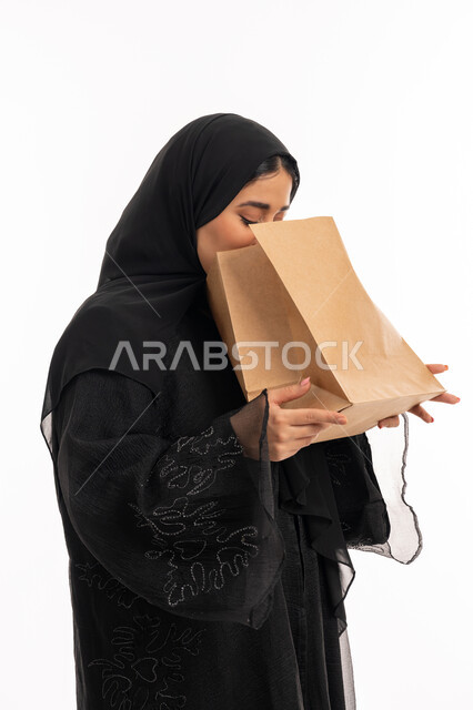 إيماءات التقيؤ والغثيان، الإحساس بالمغص والوجع، الحاجه للمساعدة وطلب العلاج، بورتريه مقرب من الجانب لامرأة عربية خليجية إماراتية ترتدي عباءة سوداء تحمل بيدها كيس ورقي، شابة سعودية مريضة، خلفية بيضاء