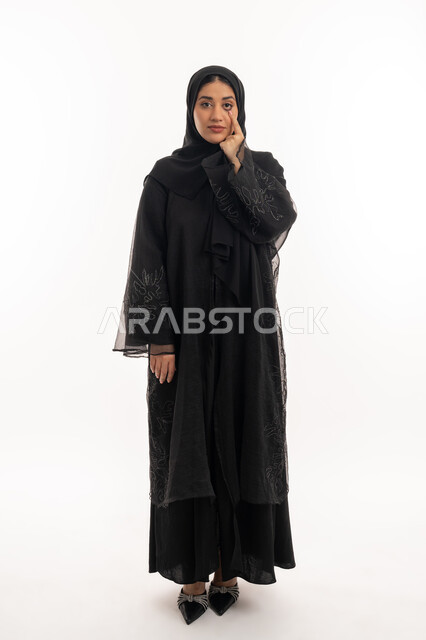Trying to see clearly, focusing on something, suffering from poor eyesight, portrait of a veiled Emirati Gulf Arab woman wearing a black abaya raising her hand to her eye, elegant Saudi young woman, full body image, white background