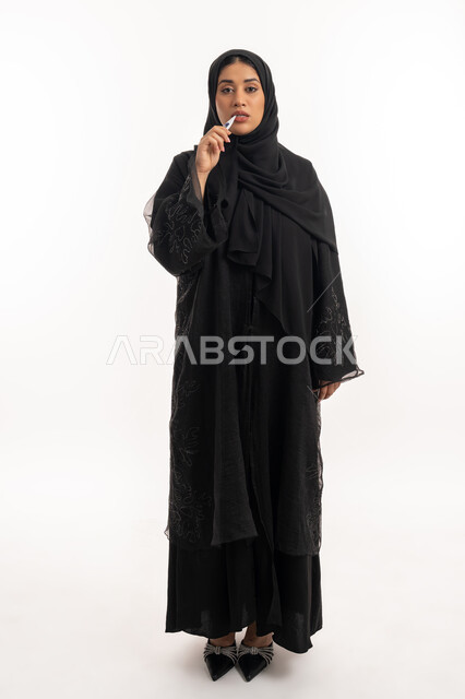 Fever and fatigue, treatment plan, feeling sick and tired, portrait of a veiled Arab Gulf Emirati woman wearing a black abaya taking her temperature using a digital thermometer, sick Saudi young woman, full body image, white background
