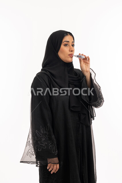 اتباع إجراءات السلامة والوقاية، الإحساس بالمرض والإرهاق، الحاجة للمساعدة وزيارة الطبيب، الإصابة بالحمى والتعب، بورتريه من الجانب لامرأة عربية خليجية اماراتية محجبة ترتدي عباءة سوداء تقوم بقياس حرارتها باستخدام الميزان الرقمي، شابة سعودية مريضة، خلفية بيضاء