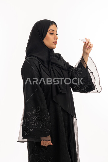وضع خطة علاجية، الحاجة للمساعدة وزيارة الطبيب، الإصابة بالحمى والتعب، الإحساس بالمرض والإرهاق، بورتريه من الجانب لامرأة عربية خليجية اماراتية محجبة ترتدي عباءة سوداء تحمل بيدها ميزان حرارة رقمي، شابة سعودية مريضة، خلفية بيضاء
