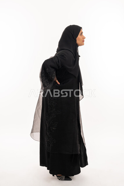 تعابير الألم ووجع الظهر، الشعور بالمرض والإرهاق، بورتريه من الجانب لامرأة عربية خليجية اماراتية محجبة ترتدي عباءة سوداء تضع يدها على ظهرها بايماءات التعب، الحاجة للعلاج والاستشارة الطبية، صورة لكامل الجسم، خلفية بيضاء