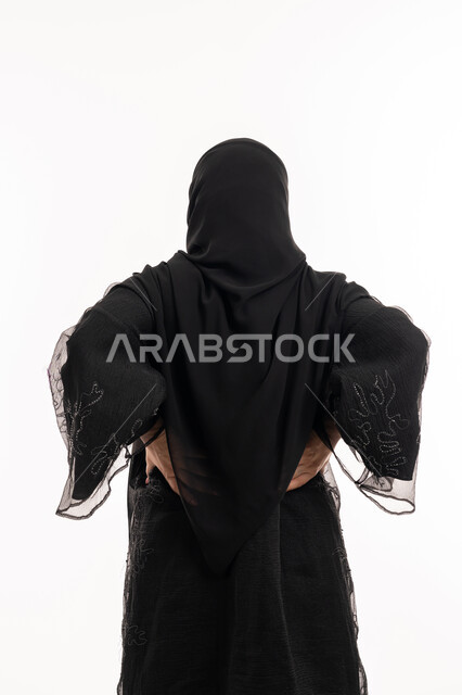 الشعور بالمرض والإرهاق، تعابير الألم ووجع الظهر، بورتريه من الخلف لامرأة عربية خليجية اماراتية محجبة ترتدي عباءة سوداء تضع يدها على ظهرها بايماءات التعب، الحاجة للعلاج والاستشارة الطبية، خلفية بيضاء