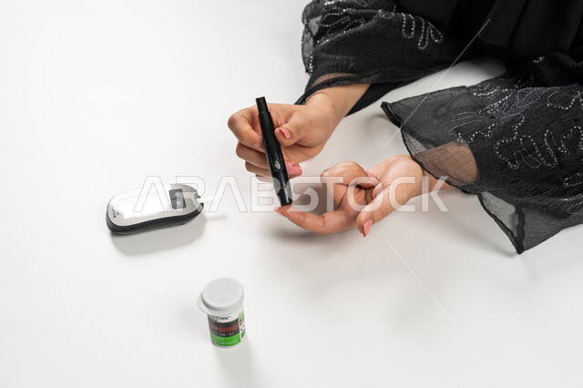 حالات مرضية ومشاكل وآلام جسدية, جهاز إلكتروني حديث لمرضى داء السكري, بورتريه علوي عامودي ليد امرأة عربية خليجية إماراتية تقوم بفحص نسبة السكر في الدم, الرعاية الصحية والفحص الطبي السريع, مشاكل ارتفاع السكر في الدم, شابة سعودية مريضة، خلفية بيضاء