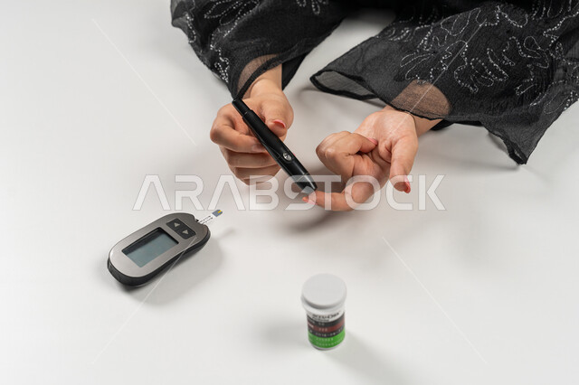 جهاز إلكتروني حديث لمرضى داء السكري, حالات مرضية ومشاكل وآلام جسدية, بورتريه علوي عامودي ليد امرأة عربية خليجية إماراتية تقوم بفحص نسبة السكر في الدم, الرعاية الصحية والفحص الطبي السريع, مشاكل ارتفاع السكر في الدم, شابة سعودية مريضة، خلفية بيضاء