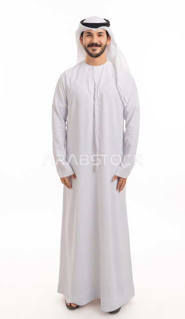 الأناقة والاهتمام بالمظهر الخارجي، الوقوف باستعداد واستقامة, مفهوم الرجولة والثقة بالنفس بورتريه لرجل عربي خليجي إماراتي مبتسم يرتدي الكندورة والغترة ينظر الى الكاميرا بتعابير السعادة والسرور، صورة الجسم بالطول الكامل, خلفية بيضاء