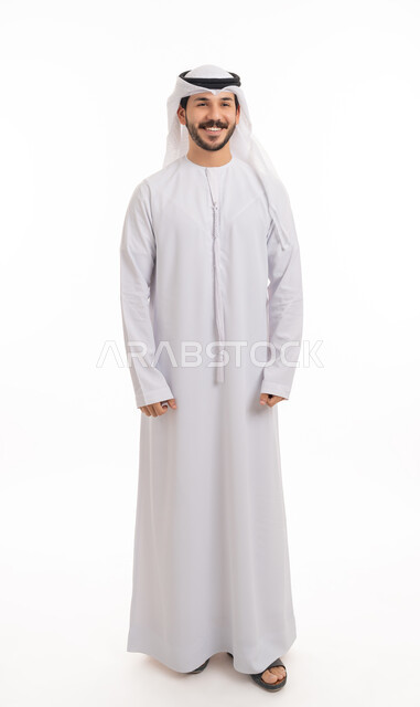الوقوف باستعداد واستقامة, مفهوم الرجولة والثقة بالنفس بورتريه لرجل عربي خليجي إماراتي مبتسم يرتدي الكندورة والغترة ينظر الى الكاميرا بتعابير السعادة والسرور، الأناقة والاهتمام بالمظهر الخارجي، صورة الجسم بالطول الكامل, خلفية بيضاء