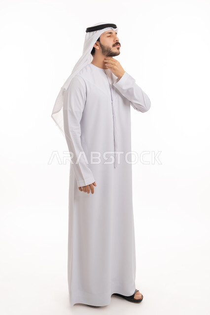 الحاجة إلى العلاج والدواء, الاحساس بألم البلعوم, مفهوم الاهتمام بالصحة, الاصابة بنزلة برد والتهاب الحلق، بورتريه لشاب عربي خليجي إماراتي يرتدي الكندورة والغترة يضع يديه على حلقه ويشعر بالاختناق, صورة الجسم بالطول الكامل, خلفية بيضاء