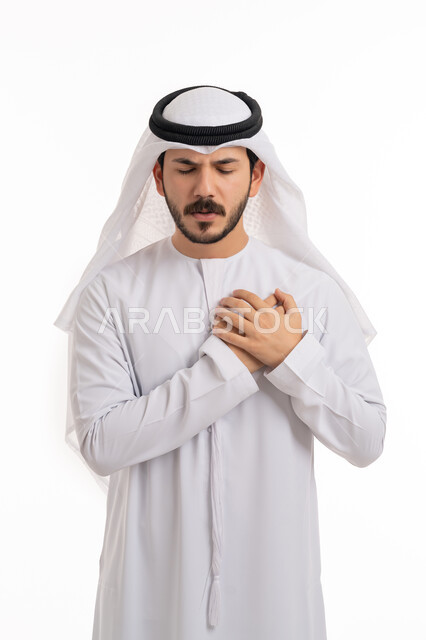 الشعور في زيادة معدل ضربات القلب, الاحساس بذبحه صدريه، بورتريه لشاب عربي خليجي اماراتي يرتدي الكندورة والغترة يضع يده على قلبه ويشعر بحالة سيئة من الوخز والألم, اضطرابات وأمراض قلبية, التعب والإرهاق والضغوطات النفسية, خلفية بيضاء