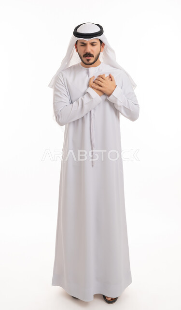 الاحساس بذبحه صدريه، بورتريه لشاب عربي خليجي اماراتي يرتدي الكندورة والغترة يضع يده على قلبه ويشعر بحالة سيئة من الوخز والألم, اضطرابات وأمراض قلبية, التعب والإرهاق والضغوطات النفسية, الشعور في زيادة معدل ضربات القلب, صورة الجسم بالطول الكامل, خلفية بيضاء