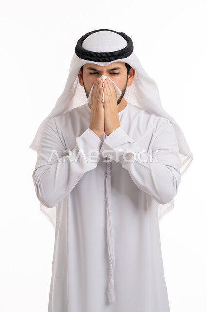 التهاب الأنف التحسسية, الشعور بالمرض و الزكام والحاجة الى العلاج والدواء, استخدام المناديل الورقيه للعطس, بورتريه لشاب عربي اماراتي خليجي يرتدي الغترة والكندورة يضع يديه على وجهه بإيماءات العطاس, خلفية بيضاء