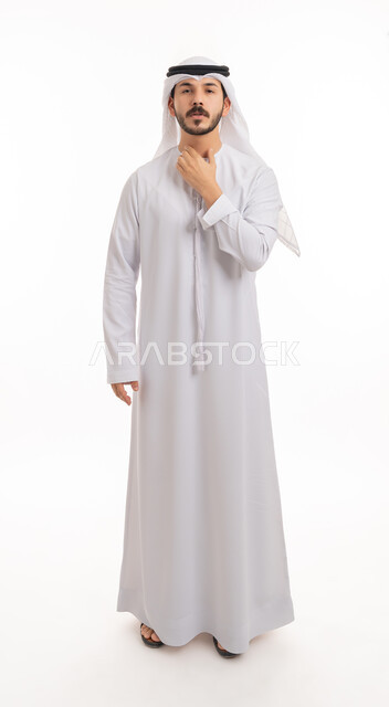 Looking at the camera with gestures of difficulty breathing, fatigue and pain, having a cold and sore throat, portrait of a young Arab Gulf Emirati man wearing a kandora and ghutra, putting his hands on his throat and feeling suffocated, severe illness and coughing, full-length body portrait, white background.