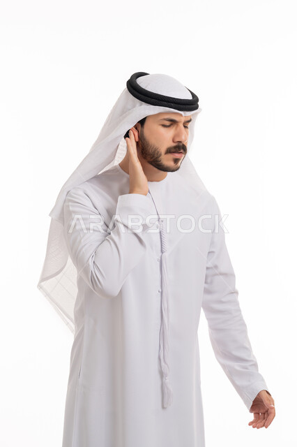 التهاب الأذن الوسطى، الحاجة للذهاب للطبيب للمساعدة و وضع خطة علاجية مناسبة، بورتريه لشاب عربي خليجي إماراتي يرتدي الكندورة والغترة يضع يده على اذنه بايماءات التألم الشديد، حالة اسعافية طارئة، خلفية بيضاء