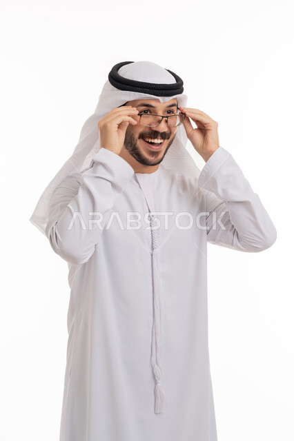 النظر إلى شيء ما ببشاشة, الشعور بالسعادة والفرح بوضوح الرؤية, استخدام النظارة الطبية لتصحيح البصر, مفهوم طول النظر وقصره, بورتريه لرجل عربي خليجي اماراتي يرتدي الكندورة والغترة يضع يديه على نظاراته, خلفية بيضاء