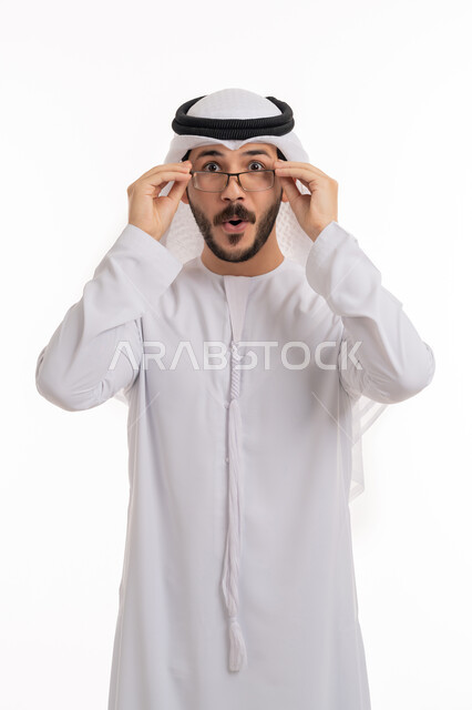 استخدام النظارة الطبية لتحسين عملية الرؤية, مفهوم طول النظر وقصره, بورتريه لرجل عربي خليجي اماراتي يرتدي الكندورة والغترة يضع يديه على نظاراته بإيماءات السرور والسعادة, الوقوف بدهشة وإعجاب, خلفية بيضاء