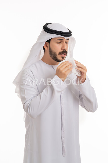التهاب الأنف التحسسية, الشعور بالزكام والحاجة الى العلاج والدواء, بورتريه لشاب عربي اماراتي خليجي يرتدي الغترة والكندورة يمسك بيده المنديل الورقي للعطس بإيماءات المرض والتعب, خلفية بيضاء