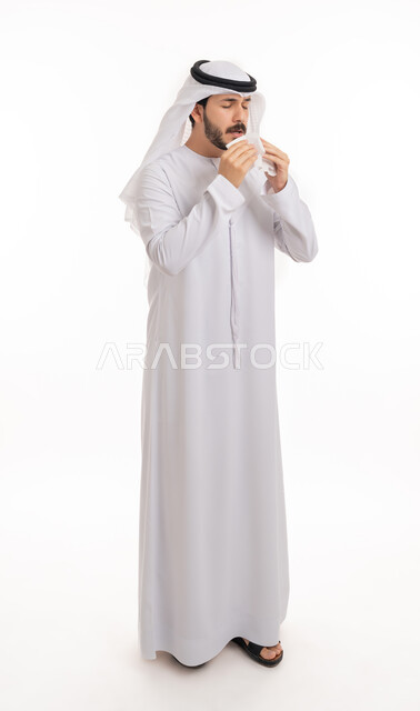 الشعور بالزكام والحاجة الى العلاج والدواء, التهاب الأنف التحسسية, بورتريه لشاب عربي اماراتي خليجي يرتدي الغترة والكندورة يمسك بيده المنديل الورقي للعطس بإيماءات المرض والتعب, صورة الجسم بالطول الكامل, خلفية بيضاء