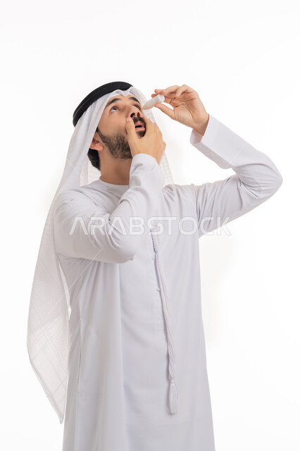 العلاج باستخدام القطرات اللازمة, الحاجة لفحص حالات التهاب العصب البصري، بورتريه لرجل عربي خليجي اماراتي يرتدي الكندورة والغترة يقوم بوضع قطرة عينية, ارتفاع ضغط العين, الاحساس بالحرقة و احمرار العيون، خلفية بيضاء