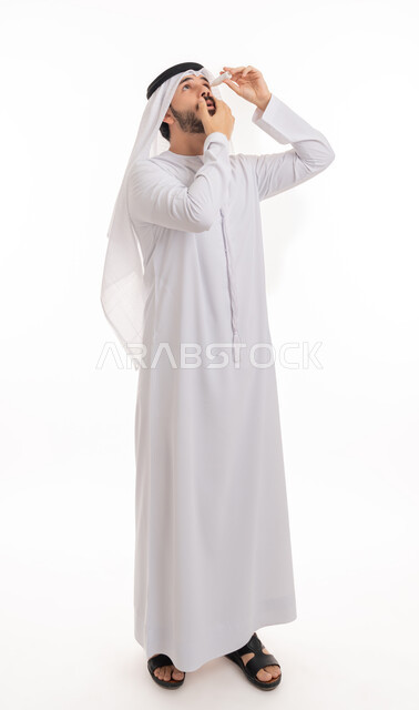 الاهتمام بالأعضاء الحساسة في الجسد, الحاجة للعلاج وفحص حالات التهاب العصب البصري، بورتريه لرجل عربي خليجي اماراتي يرتدي الكندورة والغترة يقوم بوضع قطرة عينية, ارتفاع ضغط العين, الاحساس بالحرقة و احمرار العيون،صورة الجسم بالطول الكامل,  خلفية بيضاء