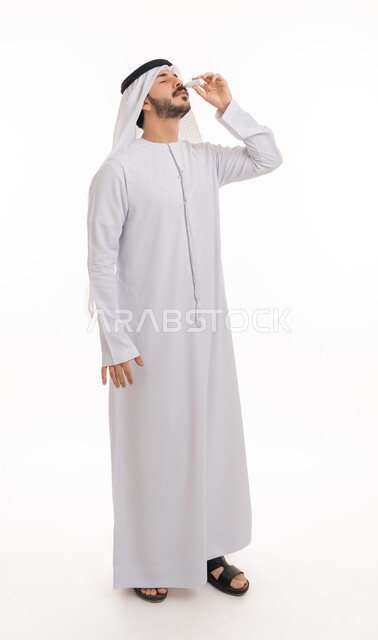 ارتفاع ضغط العين, الاحساس بالحرقة و احمرار العيون، الحاجة للفحص وعلاج حالات التهاب العصب البصري، بورتريه لرجل عربي خليجي اماراتي يرتدي الكندورة والغترة يقوم بوضع قطرة عينية, صورة الجسم بالطول الكامل, خلفية بيضاء