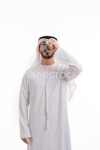 الاصابة بمشاكل التحسس الجوي, البخاخات العلاجية للأمراض التحسسية,  أجهزة استنشاق المخصصة للمرضى, المحافظة على ممر هوائي منتظم، بورتريه لرجل عربي خليجي اماراتي يرتدي الكندورة والغترة الاماراتية يحمل بيده جهاز الرذاذ الخاص بمرض الربو، خلفية بيضاء