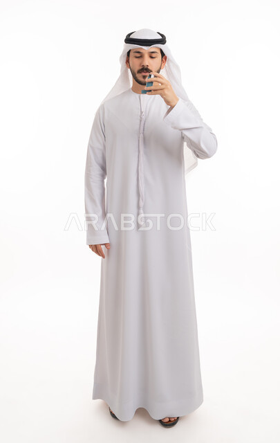المحافظة على ممر هوائي منتظم، مشاكل في الجهاز التنفسي، بورتريه لرجل عربي خليجي اماراتي يرتدي الكندورة والغترة الاماراتية يحمل بيده جهاز الرذاذ الخاص بمرض الربو، أجهزة استنشاق المخصصة للمرضى، صورة الجسم بالطول الكامل, خلفية بيضاء