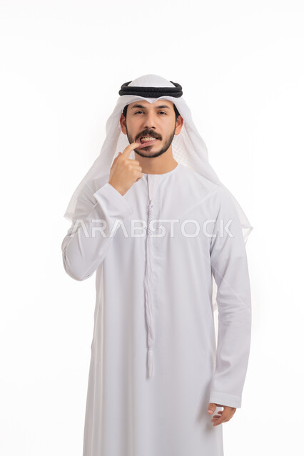 طلب العلاج والمساعدة, الحاجة لزيارة طبيب الأسنان, النظر إلى الكاميرا بانزعاج, مشاكل التهاب اللثة, بورتريه لرجل عربي خليجي اماراتي يرتدي الكندورة والغترة يضع يده على فمه يإيماءات الشعور بألم في السن, خلفية بيضاء