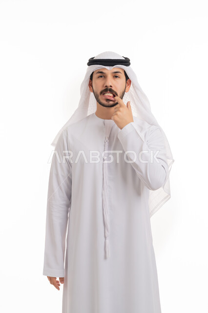 النظر إلى الكاميرا بانزعاج, مشاكل التهاب اللثة, طلب العلاج والمساعدة, الحاجة لزيارة طبيب الأسنان, بورتريه لرجل عربي خليجي اماراتي يرتدي الكندورة والغترة يضع يده على فمه يإيماءات الشعور بألم في السن, خلفية بيضاء