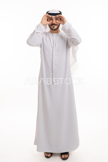 تقريب الأشياء البعيدة, المعاناة من ضعف البصر، التركيز بالنظر على شيء معين، محاولة الرؤية بوضوح، بورتريه لرجل عربي خليجي إماراتي يرتدي الكندورة والغترة يرفع يديه على شكل نظارات, صورة الجسم بالطول الكامل, خلفية بيضاء