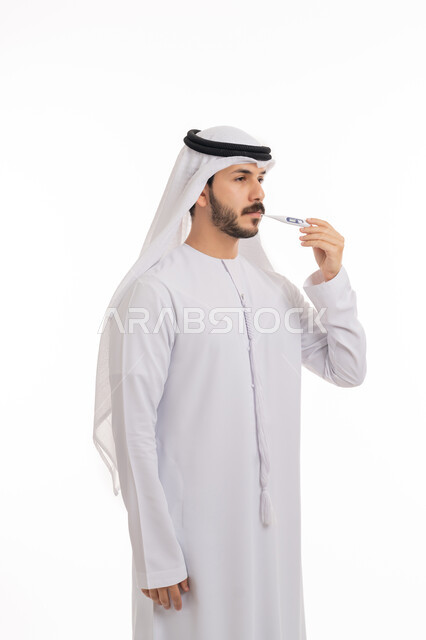 الحاجة إلى زيارة الطبيب للمساعدة ووضع خطة علاجية, الإصابة بالحمى والتعب, الإحساس بالمرض والإرهاق، بورتريه لشاب عربي خليجي اماراتي يرتدي الكندورة والغترة يقوم بقياس حرارته باستخدام الميزان الرقمي، خلفية بيضاء