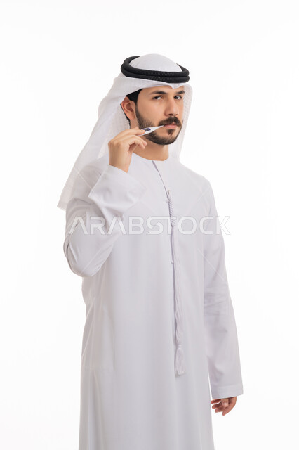 أعراض الاصابة بالحمى والتعب الجسدي, الوقوف بانزعاج والنظر إلى الكاميرا, بورتريه لرجل عربي خليجي اماراتي يرتدي الكندورة والغترة الاماراتية يقوم بقياس درجة حرارته باستخدام الميزان الرقمي, مفهوم الاهتمام بالصحة, خلفية بيضاء