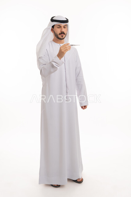 مفهوم الاهتمام بالصحة الجسدية, ضرورة زيارة الطبيب لوضع الخطة العلاجية، الإحساس بالمرض والإرهاق، بورتريه لشاب عربي خليجي إماراتي يرتدي الكندورة والغترة ينظر إلى مؤشر الميزان الرقمي بتعابير الانزعاج والتعب، صورة الجسم بالطول الكامل, خلفية بيضاء