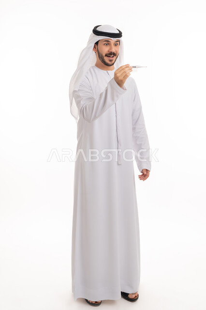 الوقوف بإيماءات الدهشة والاستغراب والذهول, بورتريه لرجل عربي خليجي اماراتي يرتدي الكندورة والغترة ينظر إلى مؤشر الميزان الرقمي لقياس الحرارة, اتباع اجراءات السلامة والمحافظة على الصحة الجسدية, صورة الجسم بالطول الكامل, خلفية بيضاء