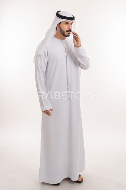 إيماءات التعب بسبب المرض, الحاجة إلى زيارة الطبيب للمساعدة ووضع خطة علاجية, الإصابة بالحمى والإرهاق، بورتريه لرجل عربي خليجي إماراتي يرتدي الكندورة والغترة يقوم بقياس حرارته باستخدام الميزان الرقمي، صورة الجسم بالطول الكامل, خلفية بيضاء