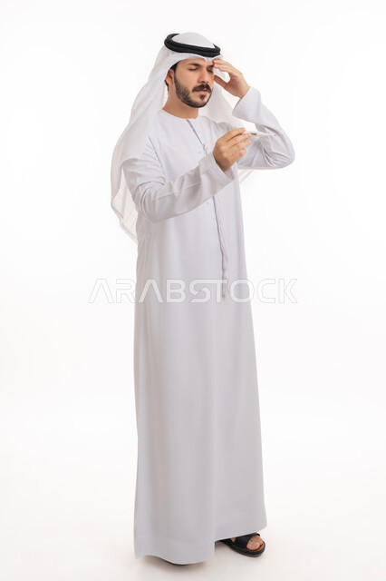 ضرورة زيارة الطبيب لوضع الخطة العلاجية، الإحساس بالمرض والإرهاق، بورتريه لشاب عربي خليجي إماراتي يرتدي الكندورة والغترة يقوم بقياس درجة حرارته بإستخدام الميزان الرقمي بتعابير الانزعاج والتعب، صورة الجسم بالطول الكامل, خلفية بيضاء