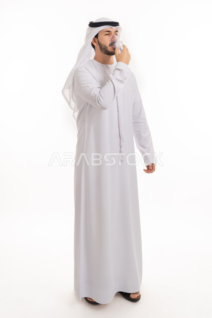استخدام جهاز التنفس الصناعي والمحافظة على ممر هوائي منتظم, بورتريه لرجل عربي إماراتي خليجي يرتدي الكندورة والغترة يقوم باستنشاق أدوية معالجة لانقطاع التنفس عن طريق قناع الاكسجين، مداواة أمراض الربو المزمنة, صورة الجسم بالطول الكامل, خلفية بيضاء