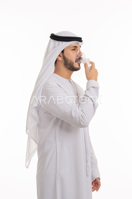 مداواة أمراض الربو المزمنة, المحافظة على ممر هوائي منتظم باستخدام جهاز التنفس الصناعي، بورتريه من الجانب لرجل عربي إماراتي خليجي يرتدي الكندورة والغترة يقوم باستنشاق أدوية معالجة لانقطاع التنفس عن طريق قناع الاكسجين، خلفية بيضاء