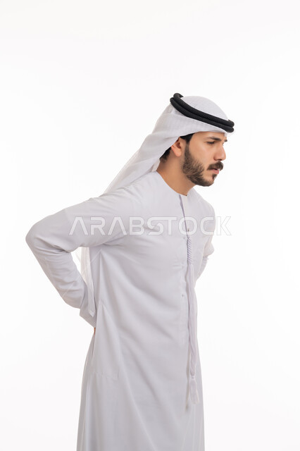 الشعور بالوجع والألم الجسدي، التعب والإرهاق والإحساس بالمرض، الحاجة إلى العلاج، آلام العامود الفقري والظهر، بورتريه من الجانب لرجل عربي خليجي إماراتي يرتدي الكندورة والغترة يضع يده على ظهره، خلفية بيضاء