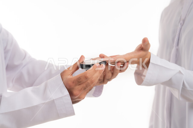 استخدام الأجهزة الالكترونية الحديثة لمرضى داء السكري, التطور العلمي والتقني في اجهزة الفحص السريعة, مفهوم الاهتمام بالصحة الجسدية, بورتريه مقرب ليد لرجل عربي خليجي إماراتي يقوم بفحص نسبة السكر في الدم, خلفية بيضاء