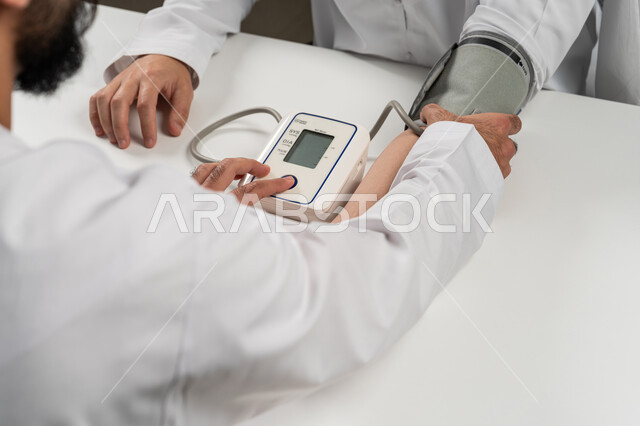 الاهتمام والعناية بالصحة الجسدية, إجراء الفحوصات الطبية السريعة, بورتريه مقرب من الخلف لرجل عربي خليجي اماراتي يرتدي الكندورة يقوم بقياس ضغط الدم للمريض باستخدام الميزان الالكتروني الحديث, مفهوم الطب والرعاية الصحية, خلفية رمادية