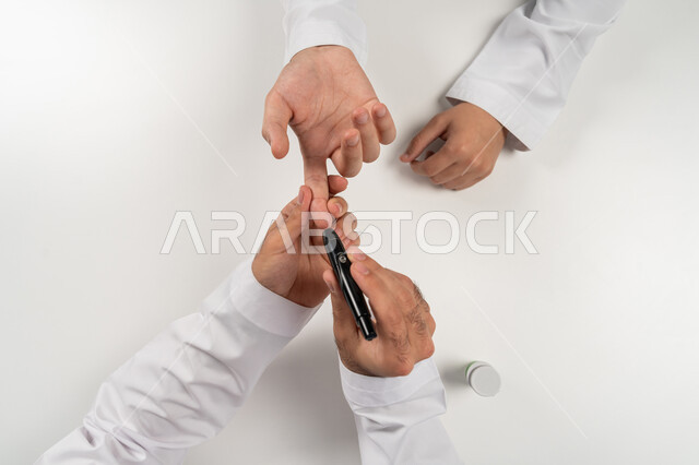 حالات مرضية ومشاكل وآلام جسدية, جهاز إلكتروني حديث لمرضى داء السكري, بورتريه مقرب علوي عامودي ليد رجل عربي خليجي إماراتي يقوم بفحص نسبة السكر في الدم, الرعاية الصحية والفحص الطبي السريع, خلفية بيضاء