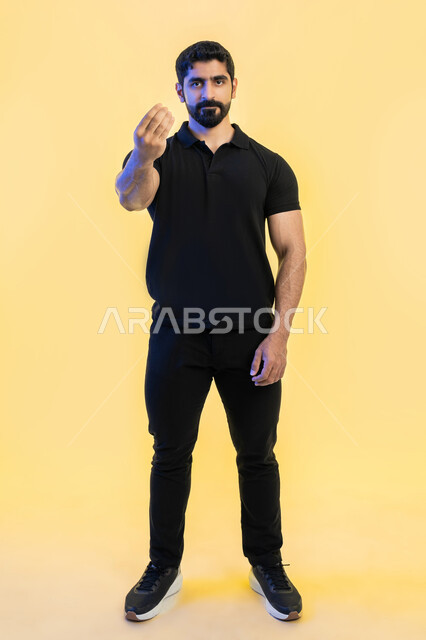 الهدوء وطلب التوقف, بورتريه لشاب  عربي خليجي اماراتي يرتدي الزي الكاجوال وينظر باتجاه الكاميرا, الاشارة بإيماءات الصبر والتأن والتريث، إمهال الوقت والإنتظار للقيام بشيء ما، صورة الجسم بالطول الكامل, خلفية صفراء
