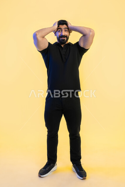 الشعور بالصدمة والذهول والانبهار، التفاجؤ والاستغراب من شيء ما،  بورتريه لشاب عربي خليجي اماراتي يرتدي الزي الكاجوال و يضع يديه على رأسه بإيماءات التعجب والدهشة، تعابير النجاح وتحقيق الأهداف, صورة الجسم بالطول الكامل، خلفية صفراء.