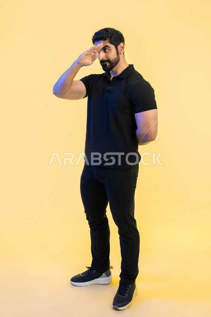 إلقاء التحية والسلام, التعبير عن الترحيب بسرور, بورتريه لرجل عربي خليجي اماراتي يرتدي الزي الكاجوال يرفع يده للأعلى لاستقبال شخص ما، صورة الجسم بالطول الكامل، خلفية صفراء