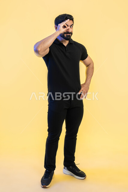 رؤية الاشياء البعيدة، بورتريه لشاب عربي خليجي اماراتي يرتدي الزي الكاجوال يضع يديه على عينه على شكل المنظار ثنائي العينين، حب المغامرة والاستكشاف، ايماءات وتعابير الدهشة والسعادة، التخطيط المستقبلي للأهداف والطموحات، صورة الجسم بالطول الكامل، خلفية صفراء