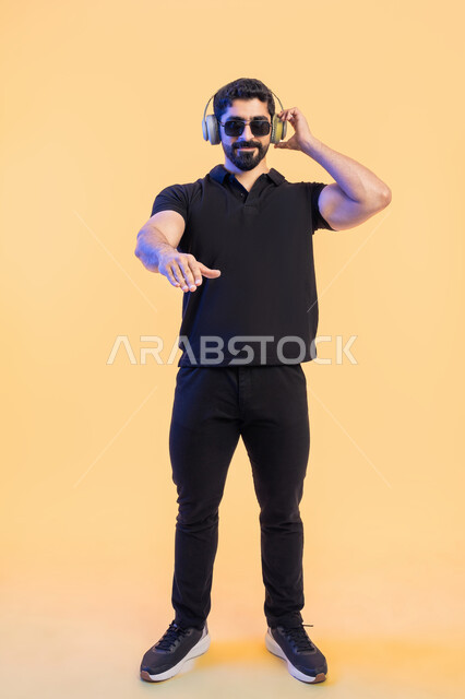 الاستماع للأغاني باسخدام الهيدفون، إيماءات وتعابير الاندماج مع الموسيقى، بورتريه لرجل عربي خليجي اماراتي يرتدي الزي الكاجوال والنظارات الشمسية يضع سماعة الرأس،  التفاعل مع الانغام الموسيقية، صورة الجسم بالطول الكامل, خلفية صفراء