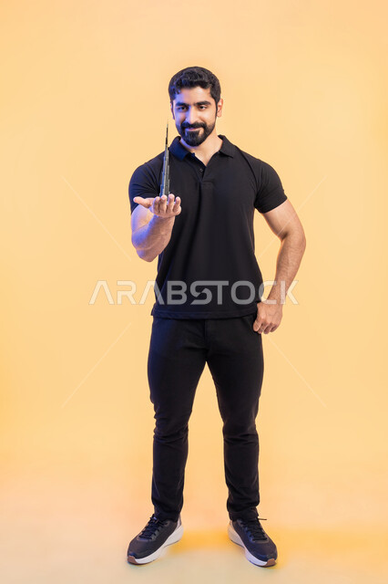 الفخر والاعتزاز بالانتماء الوطني للإمارات العربية المتحدة, معالم سياحية ترفيهية مشهورة، بورتريه لشاب عربي خليجي اماراتي يرتدي الزي الكاجوال يحمل بيده مجسم ثلاثي الابعاد لبرج خليفة الشهير، الأبراج الشاهقة وناطحات السحاب، صورة الجسم بالطول الكامل، خلفية صفراء