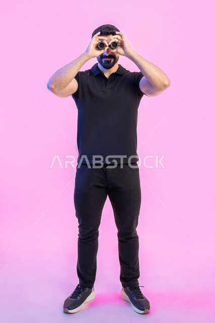 The joy of exploration and adventure, a close-up portrait of a smiling Arab Gulf Emirati young man wearing a casual outfit holding a telescope in his hand, expanding the field of view through binoculars, researching, planning and looking to the future, full-length body photos, pink background
