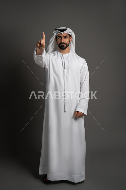 اشارة تمثل الرقم واحد ,تعابير التحذير والتنبيه, الوقوف باستقامة بإيماءات الاستفسار والاشارة إلى شيء ما, بورتريه لرجل عربي خليجي اماراتي مبتسم يرتدي الغترة و الكندورة يرفع اصبعه عاليا, صورة الجسم بالطول الكامل, خلفية سوداء
